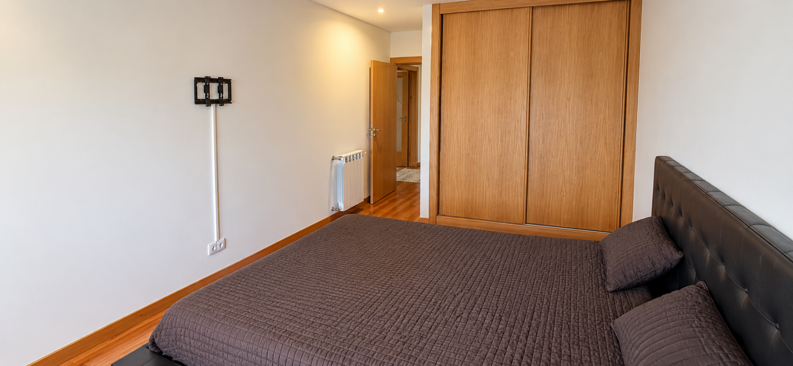 quarto-minimalista-com-cama-escura-e-madeirapng